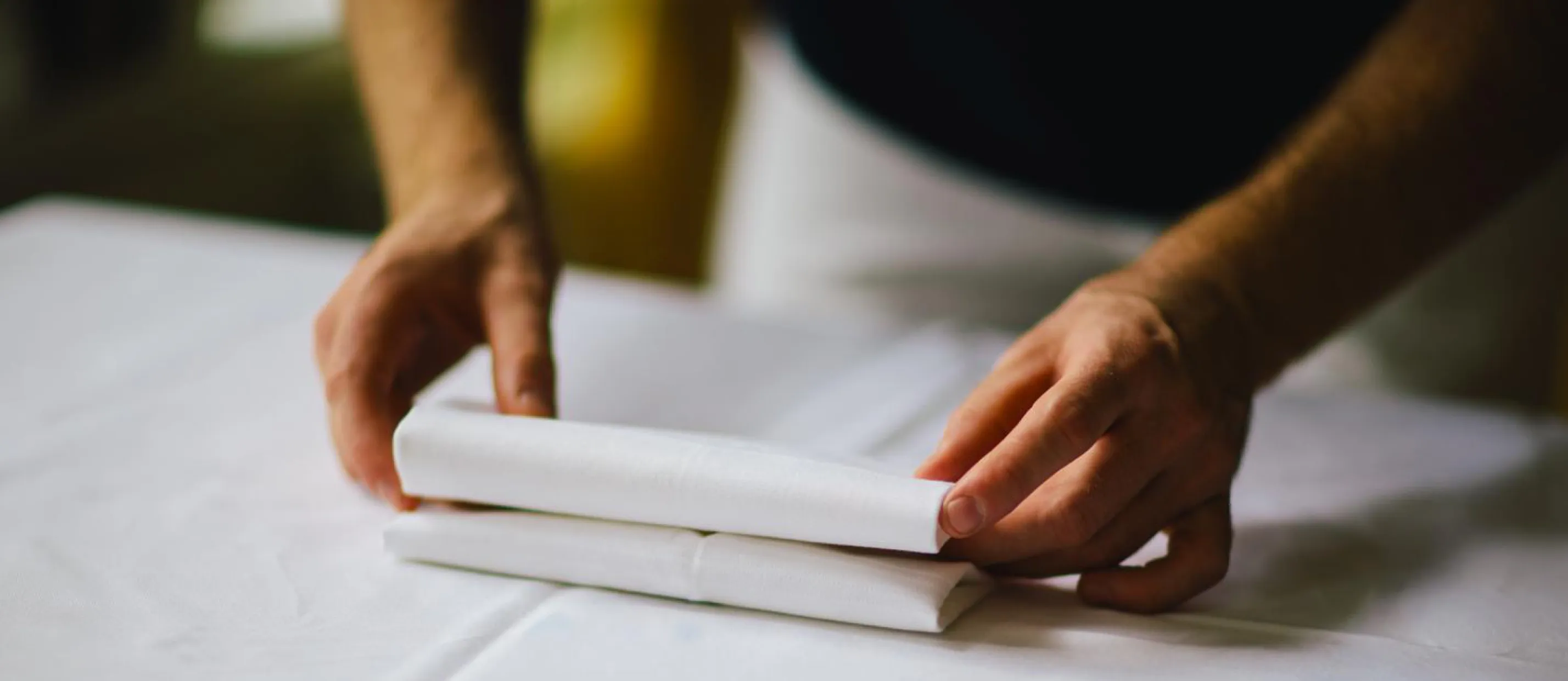 Hands folding a napkin on a white tablecloth