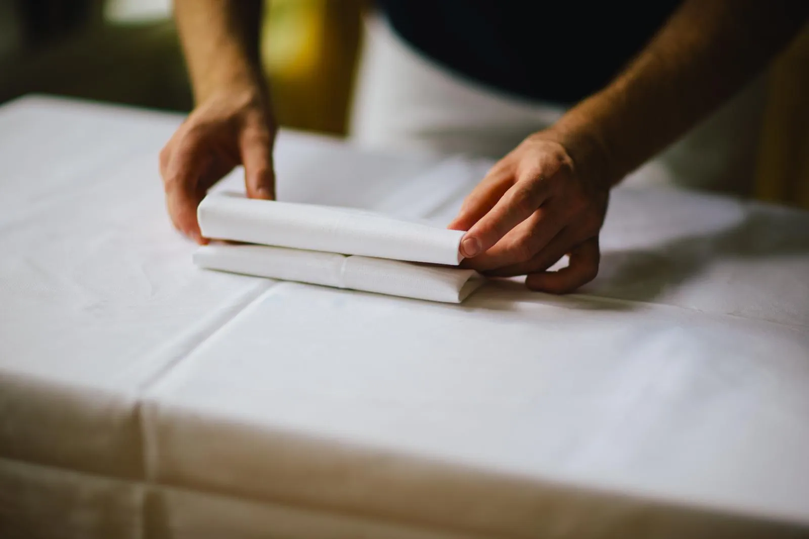 Hands folding a napkin on a white tablecloth
