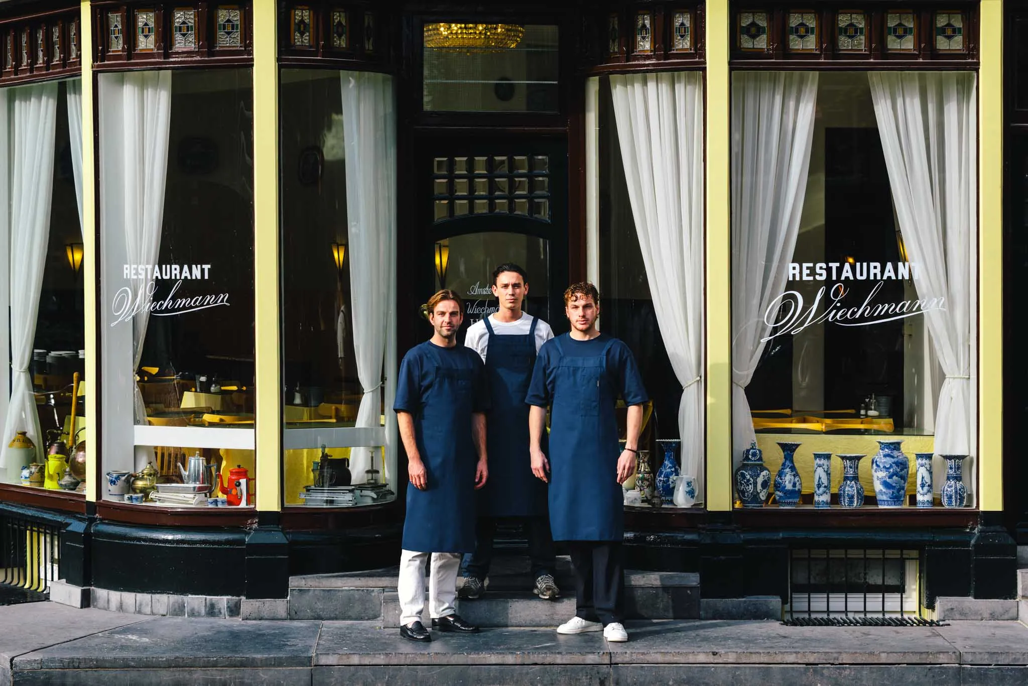 Three staff members in blue aprons in front of the windows of Restaurant Wiechmann